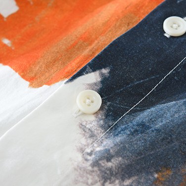 Detail of the button placket where a burnt orange stroke meets deep charcoal.